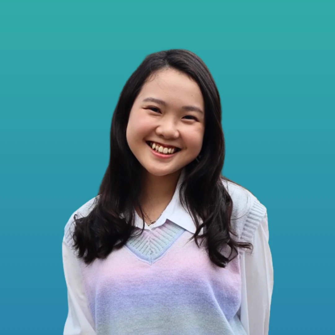 Abby is smiling. She has long hair. Wearing a whitish blue shirt with oversize shirt on top.