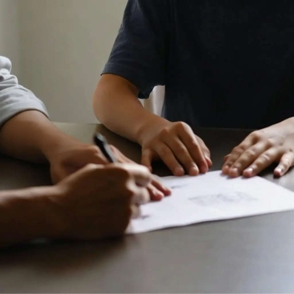 Two adults sitting at a table as one writes on a form during a psychological assessment.