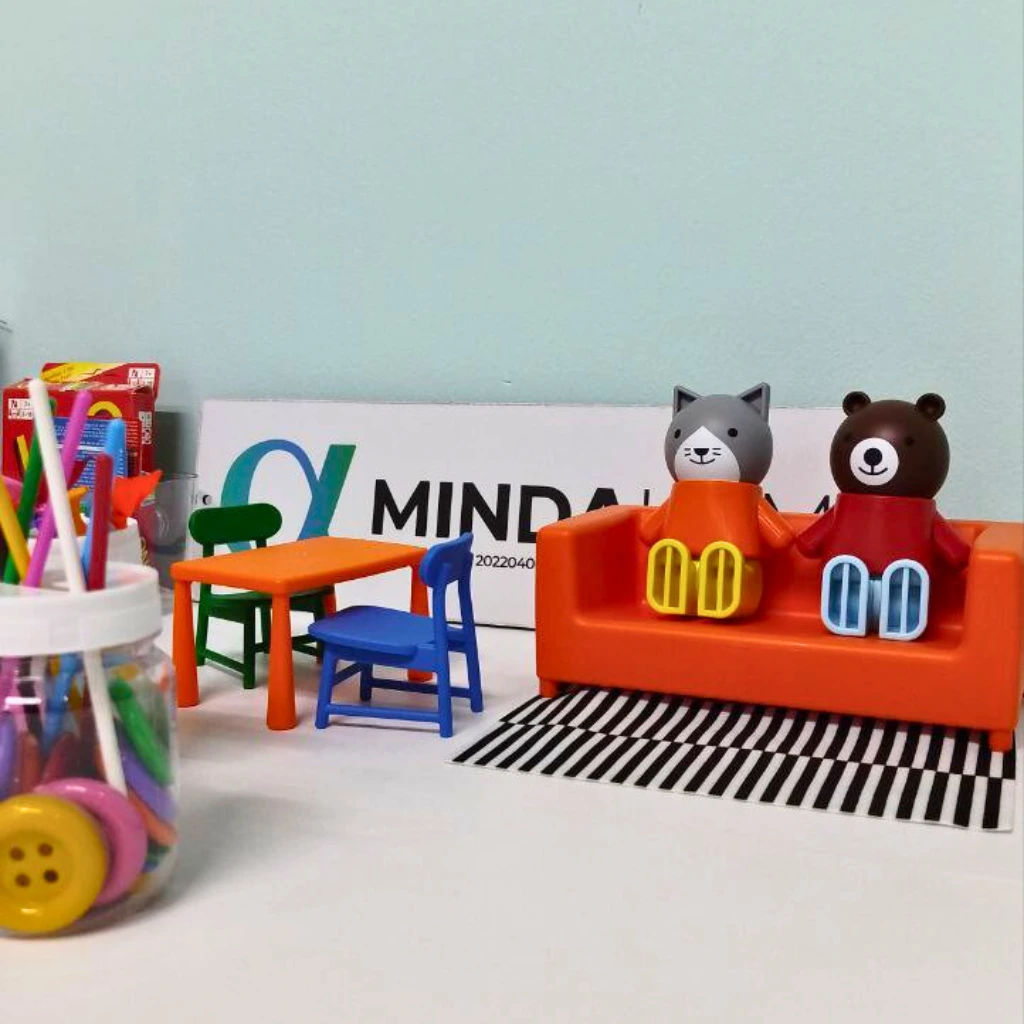 Miniature room scene with toy figures on an orange couch and small furniture.
