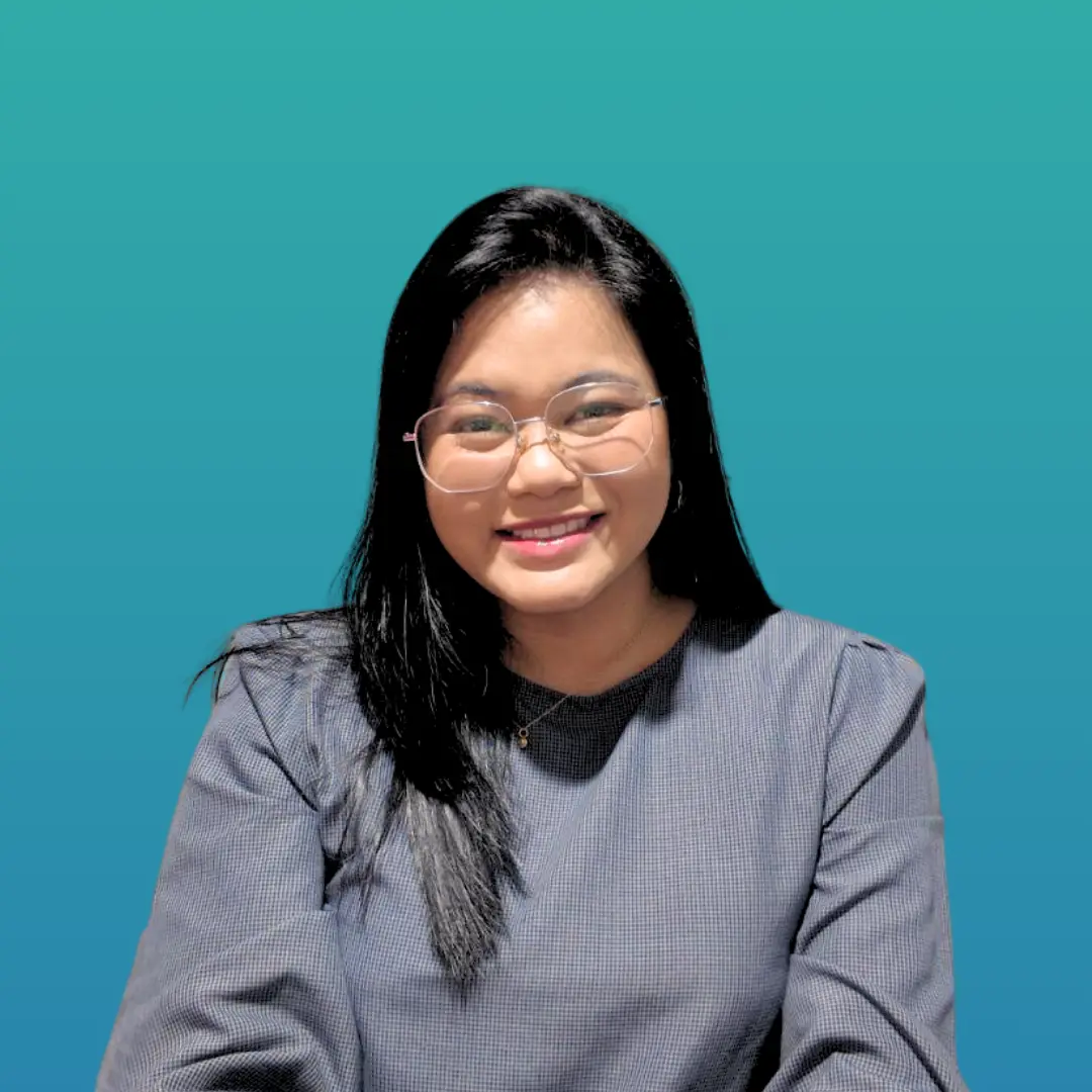 A person with long dark hair and glasses smiling while seated against a teal background.